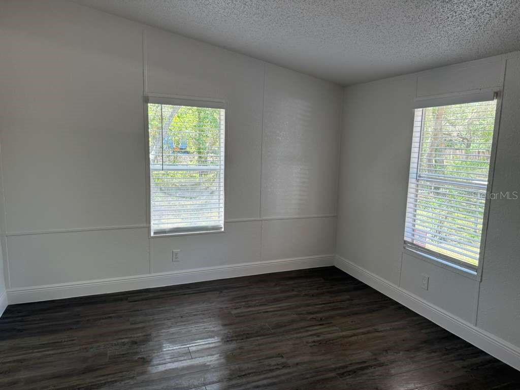 An empty room features white paneled walls, dark wood-look flooring, and two windows with blinds — 10350 EVERGREEN STREET, NEW PORT RICHEY, FL
