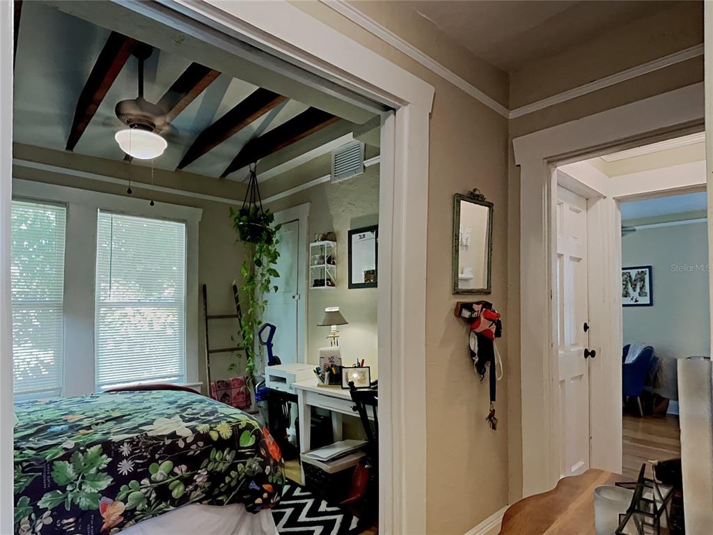 A bedroom with a floral bedspread and ceiling beams connects to a hallway with a mirror — 807 1/2 S FREMONT AVENUE UNIT #Upper, TAMPA, FL