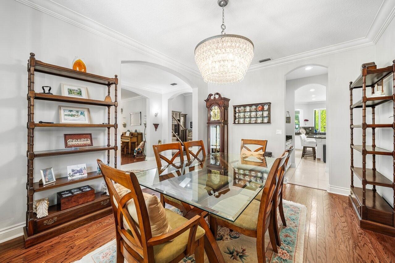 A dining room features a glass-topped table, wooden chairs, a chandelier, and two tall shelves — 6990 Cypress Cove Circle, Jupiter FL 33458, JUPITER, FL