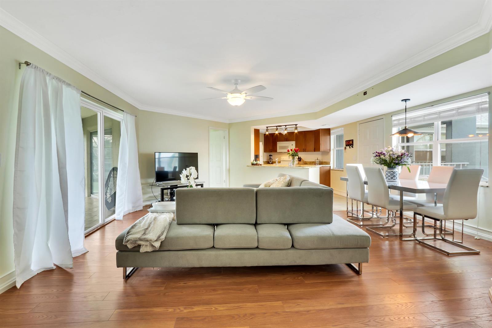 A living room with a grey sofa, hardwood floors, and an open kitchen and dining area — 3296 SE Aster Lane, Stuart FL 34994, STUART, FL