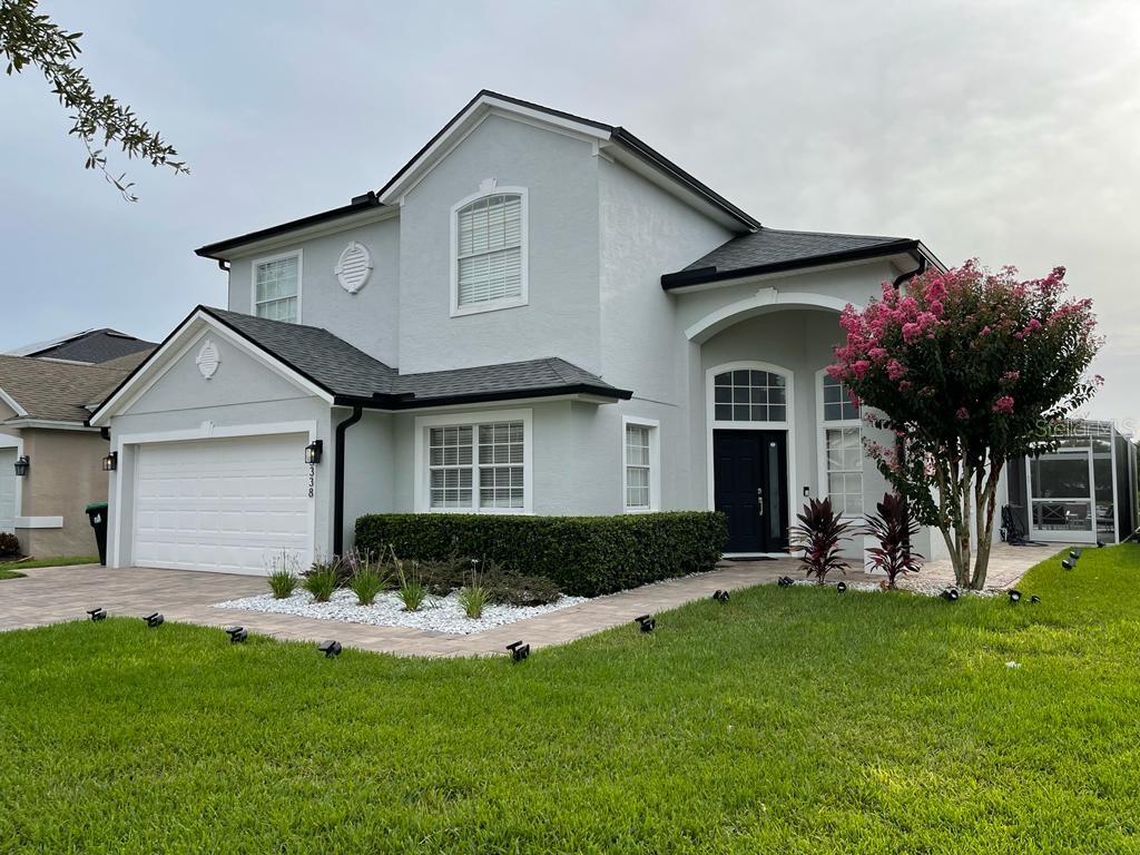 A two-story light gray house with a white garage, dark roof, and a blooming tree — 5338 LOS PALMA VISTA DRIVE, ORLANDO, FL