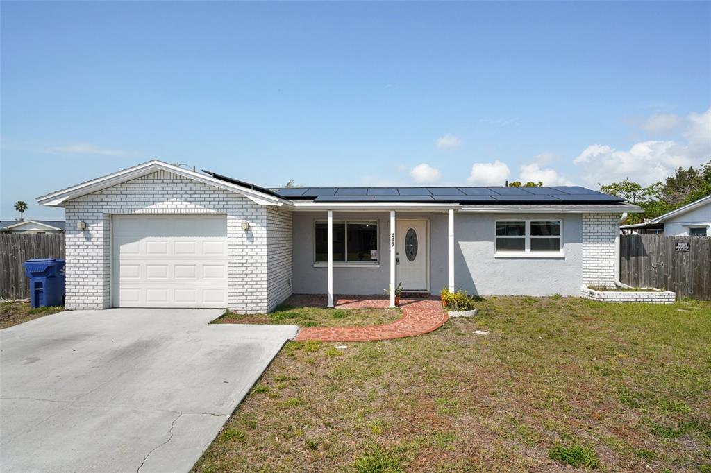 A single-story house with a white brick garage, gray stucco exterior, and rooftop solar panels — 3207 COLDWELL DRIVE, HOLIDAY, FL