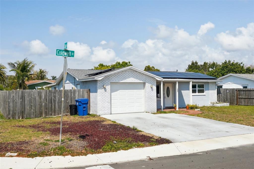 A single-story house with a white brick facade, a garage, and solar panels on the roof — 3207 COLDWELL DRIVE, HOLIDAY, FL