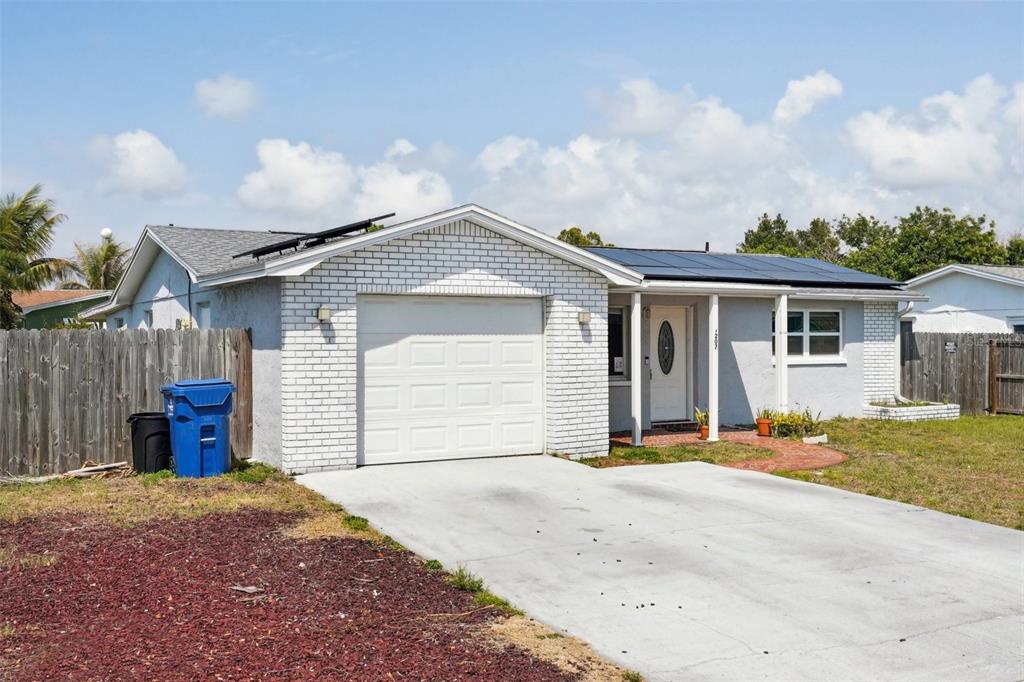 A single-story house with a white brick garage, gray stucco walls, and rooftop solar panels — 3207 COLDWELL DRIVE, HOLIDAY, FL