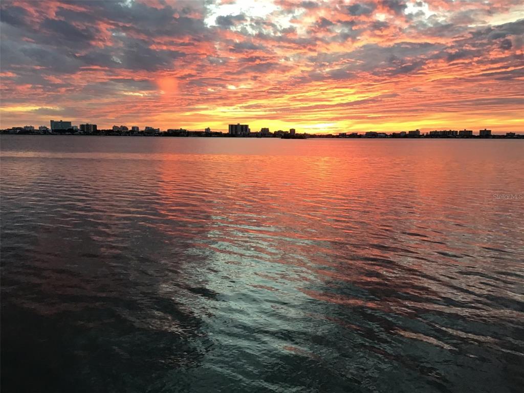 A vibrant sunset glows over a calm body of water with a distant city skyline — 1832 VENETIAN POINT DRIVE, CLEARWATER, FL