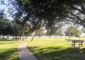 A paved walkway winds through a grassy park with mature trees and wooden benches — 5080 MONTEGO LANE, PORT CHARLOTTE, FL