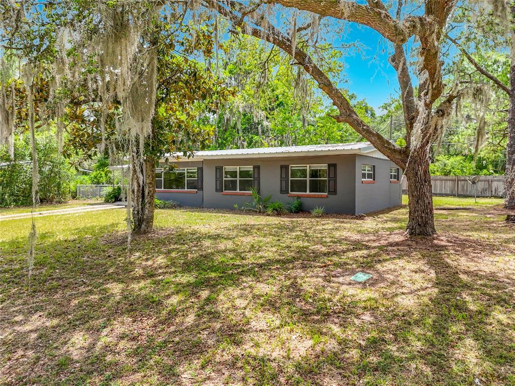 A single-story gray house with a metal roof sits on a grassy, tree-shaded lot — 414 NW 36TH TERRACE, GAINESVILLE, FL
