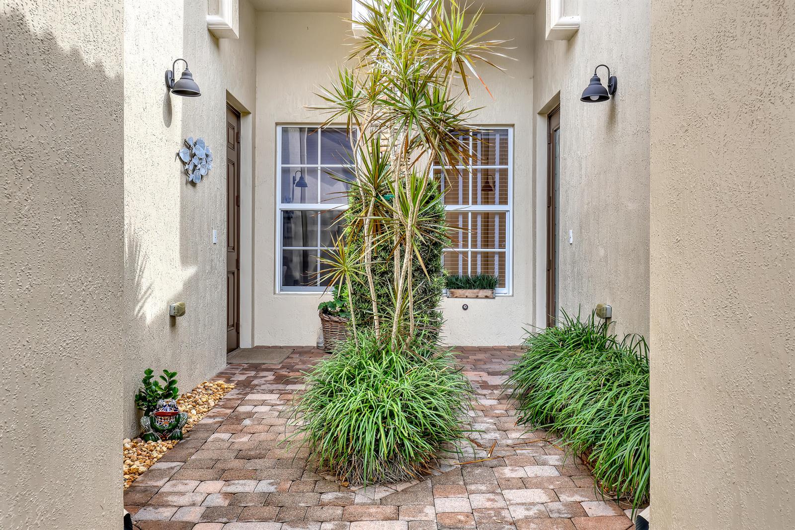 A paved courtyard features a central planter with a tall palm and surrounding green plants — 14804 Via Porta, Delray Beach FL 33446, DELRAY BEACH, FL