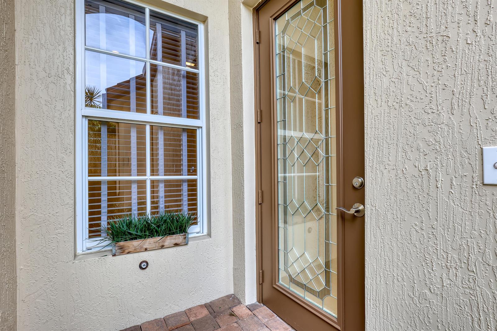 A brown door with a decorative glass insert sits beside a window with a planter — 14804 Via Porta, Delray Beach FL 33446, DELRAY BEACH, FL
