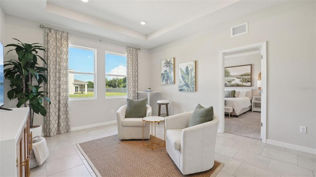 A sitting room features two white armchairs, a small table, and a view into a bedroom — 2058 STRATTEN DRIVE, ZEPHYRHILLS, FL