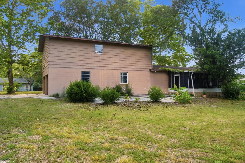 A two-story house with tan siding, a screened-in porch, and a large grassy yard — 2805 NE 24TH COURT, OCALA, FL