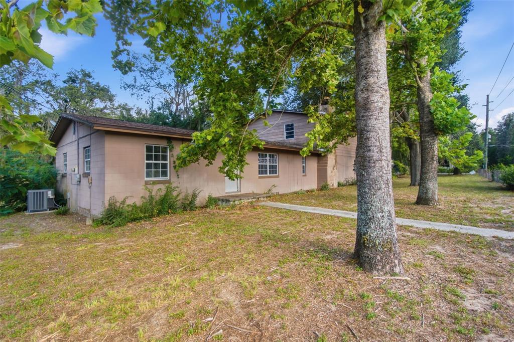 A tan, two-story house with a concrete block exterior sits on a grassy, tree-filled lot — 2805 NE 24TH COURT, OCALA, FL