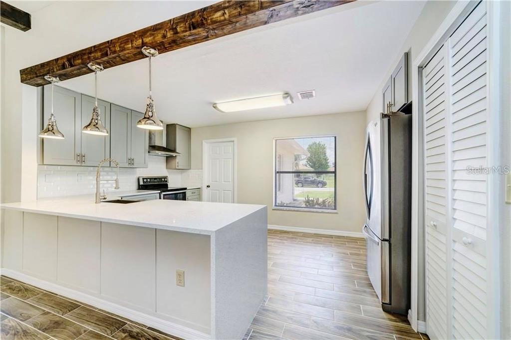 A kitchen features a white quartz island, gray cabinets, stainless appliances, and a rustic wood beam — 612 ESTRADA LANE, KISSIMMEE, FL