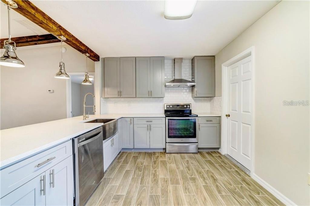 A kitchen features gray cabinets, stainless steel appliances, white countertops, and wood-look tile flooring — 612 ESTRADA LANE, KISSIMMEE, FL