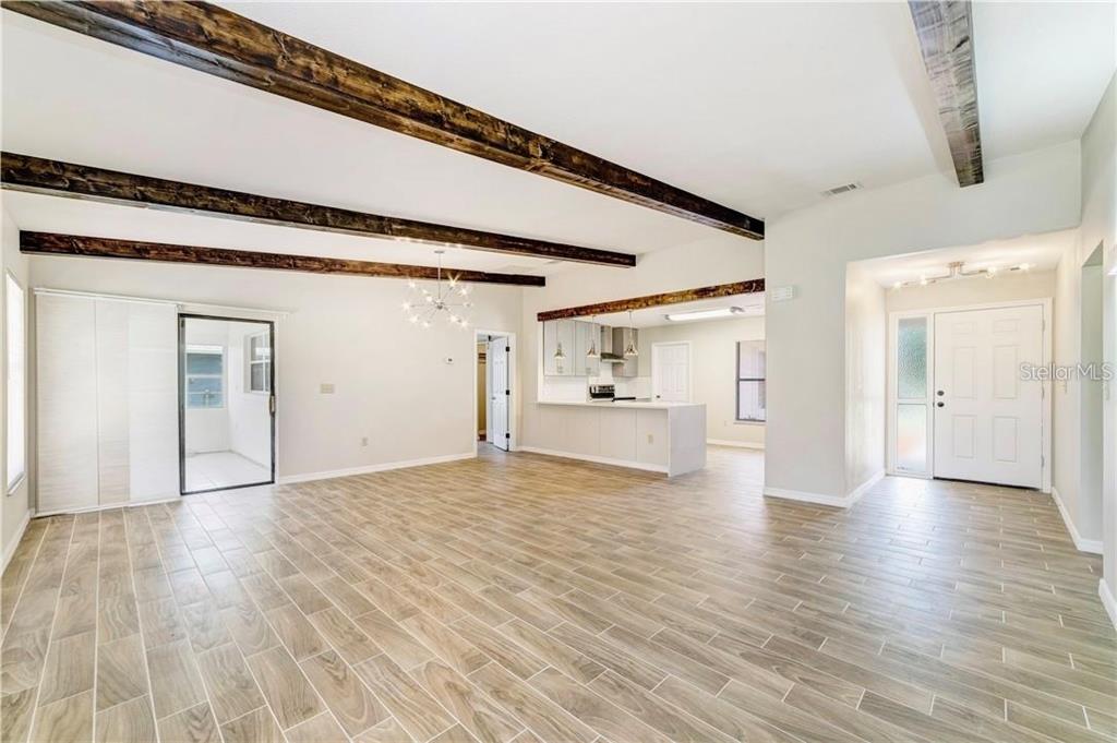 A living room with wood-look tile flooring, exposed ceiling beams, and an open kitchen — 612 ESTRADA LANE, KISSIMMEE, FL