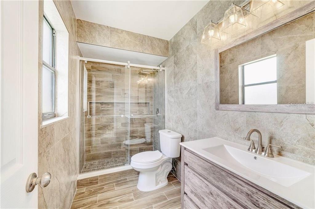 A bathroom features a glass-enclosed shower, a white toilet, and a wood-toned vanity with tile — 612 ESTRADA LANE, KISSIMMEE, FL