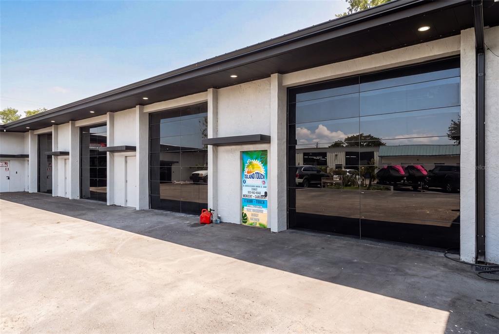 An exterior view of a commercial building featuring multiple glass garage doors and white walls — 501 INTERSTATE COURT, SARASOTA, FL