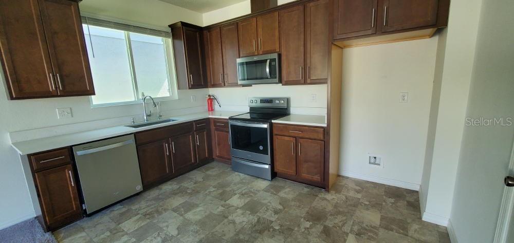 A kitchen with dark wood cabinets and stainless steel appliances opens into a carpeted living area — 2354 TWIN FLOWER LANE, SANFORD, FL