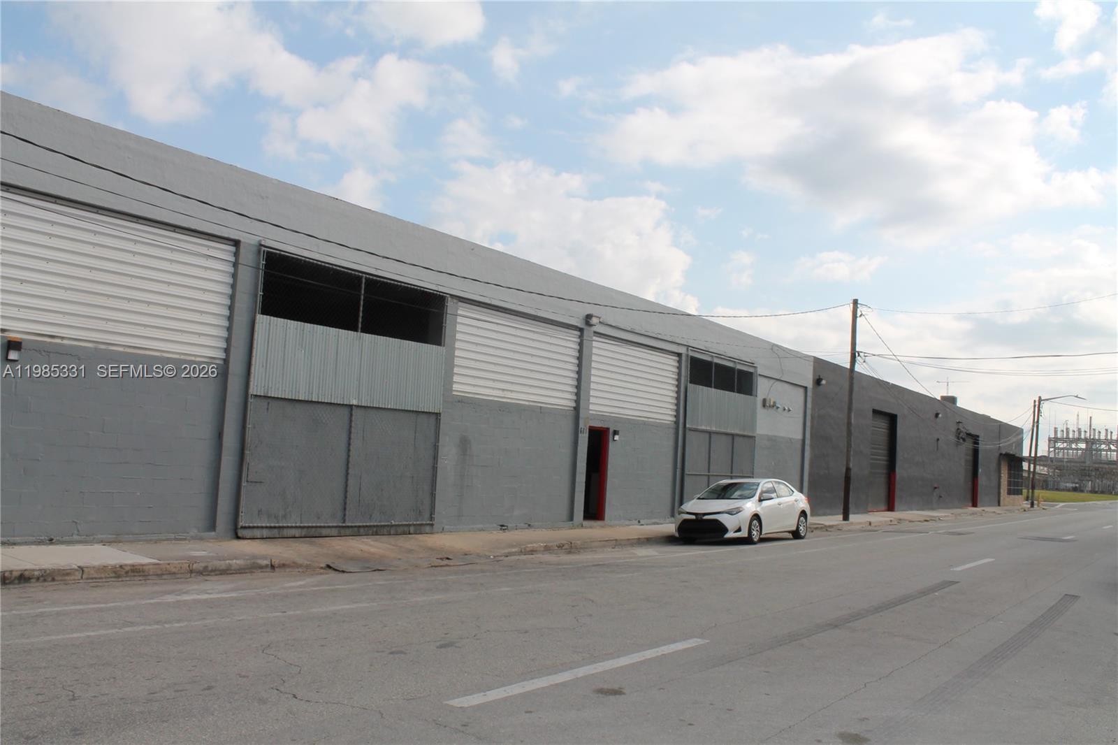A long, gray industrial warehouse building sits along a street with a white car parked — 611 NW 11th St, Miami FL 33136, MIAMI, FL