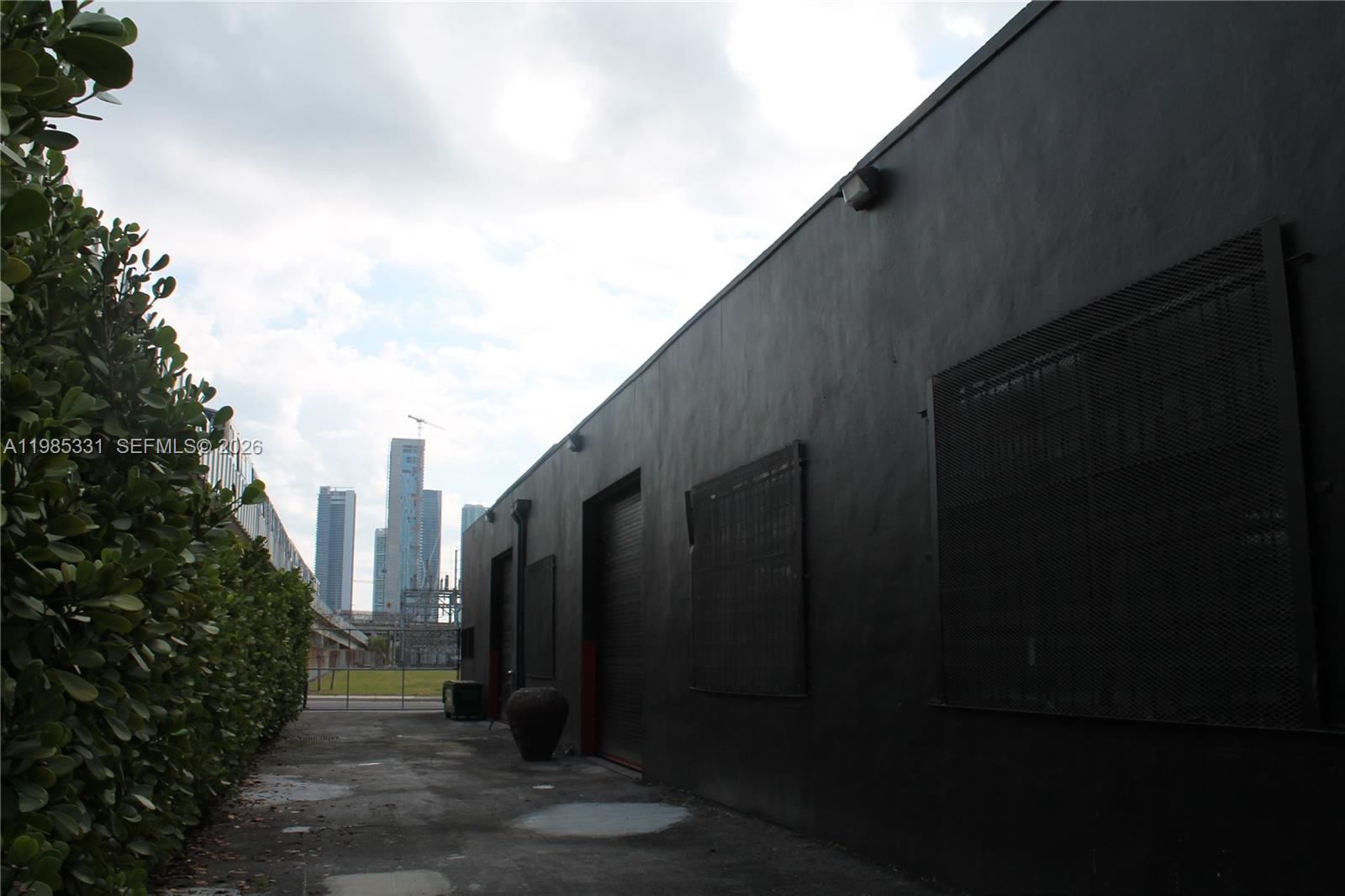 A black exterior wall with metal-grated windows runs alongside a paved path and greenery — 611 NW 11th St, Miami FL 33136, MIAMI, FL