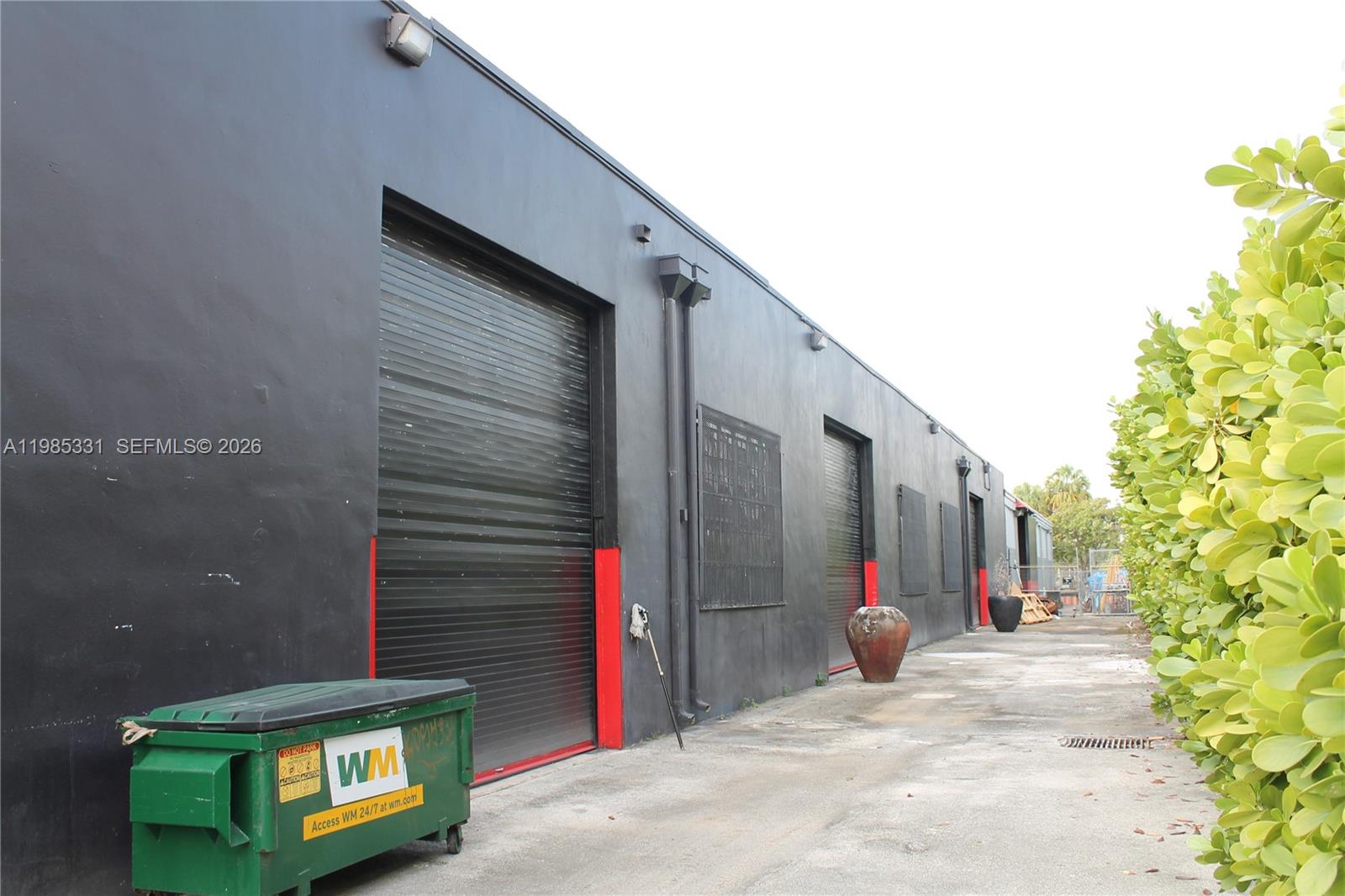 A black industrial building exterior features multiple roll-up doors and a green dumpster — 611 NW 11th St, Miami FL 33136, MIAMI, FL