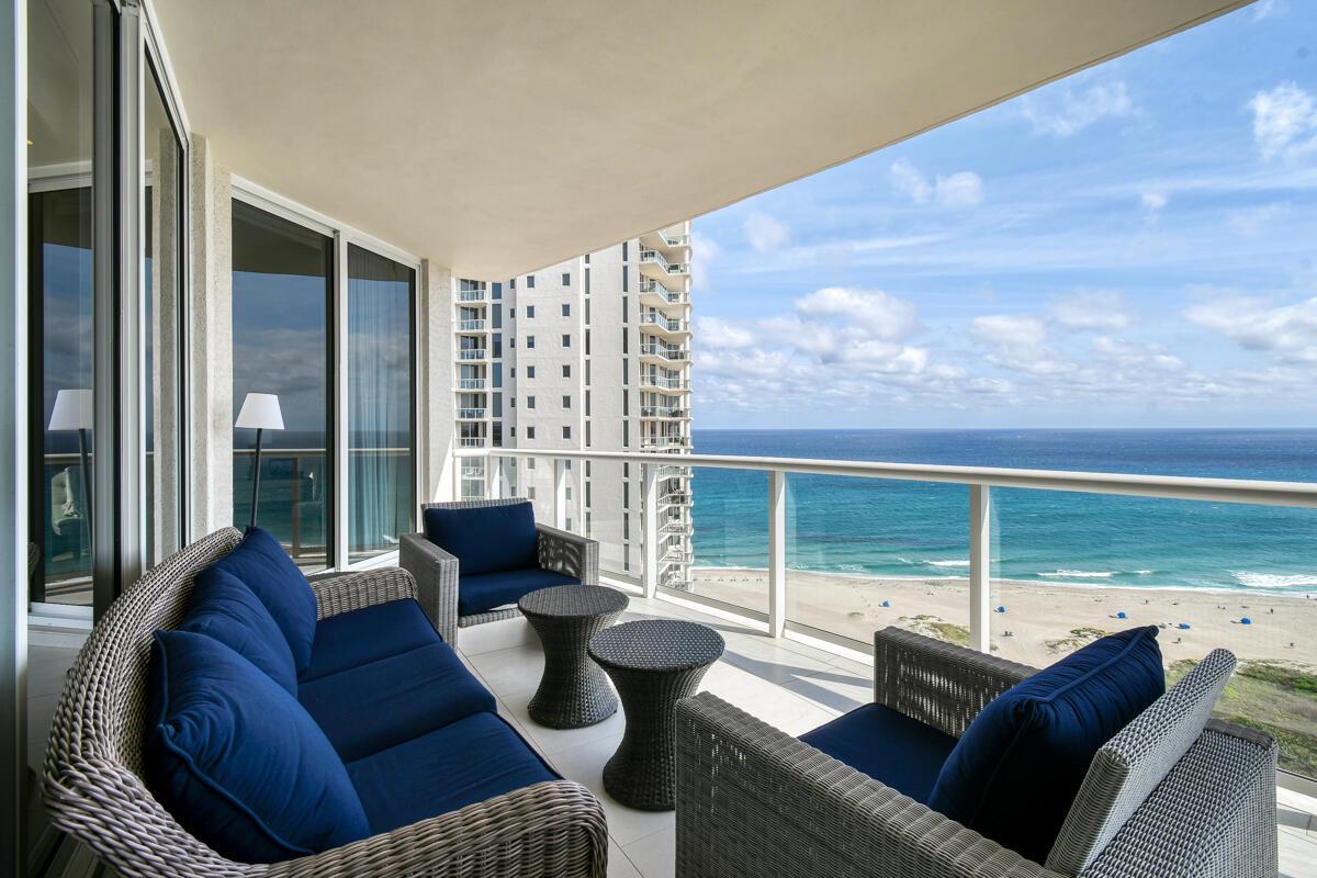 A balcony with wicker furniture overlooks the ocean and a neighboring high-rise building — 2700 N Ocean Drive # 2003b, Singer Island FL 33404, SINGER ISLAND, FL