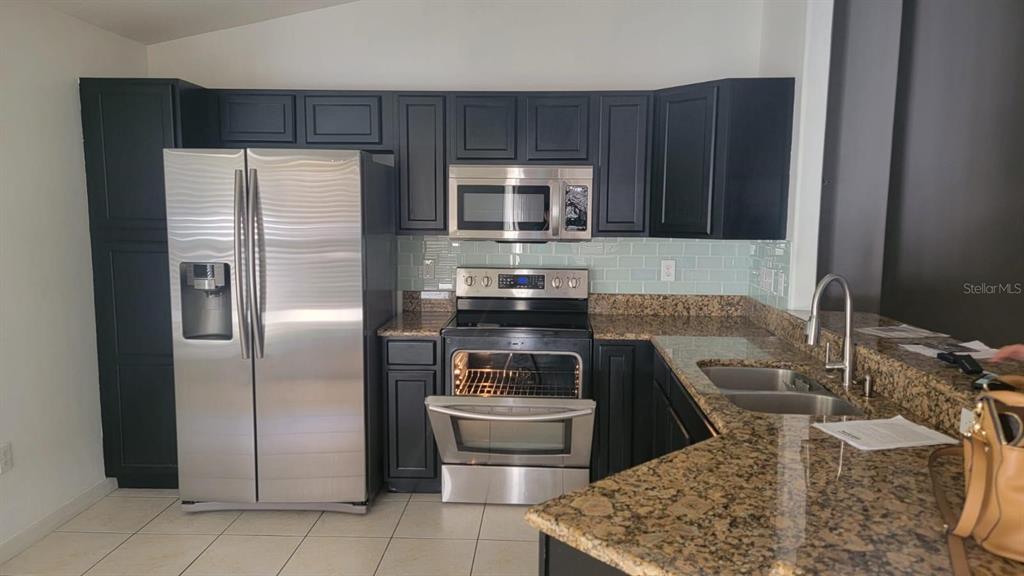 A kitchen features dark cabinets, stainless steel appliances, granite countertops, and a light blue backsplash — 7249 TWIN CEDAR LANE, LAKELAND, FL