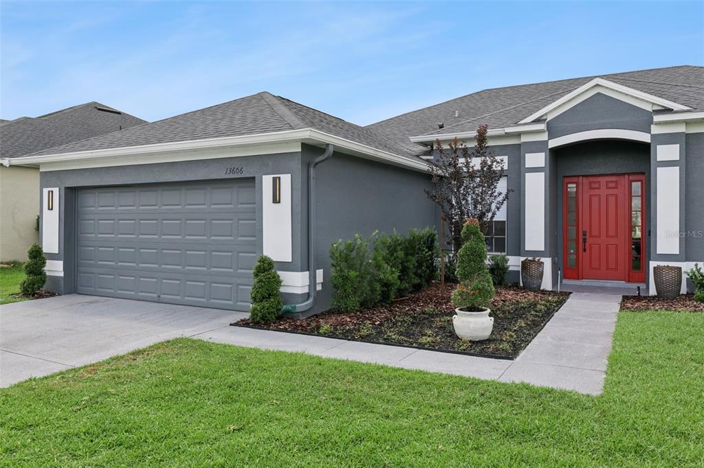 A gray single-story house features a two-car garage, a red front door, and landscaping — 13606 SUMMER RAIN DRIVE, ORLANDO, FL