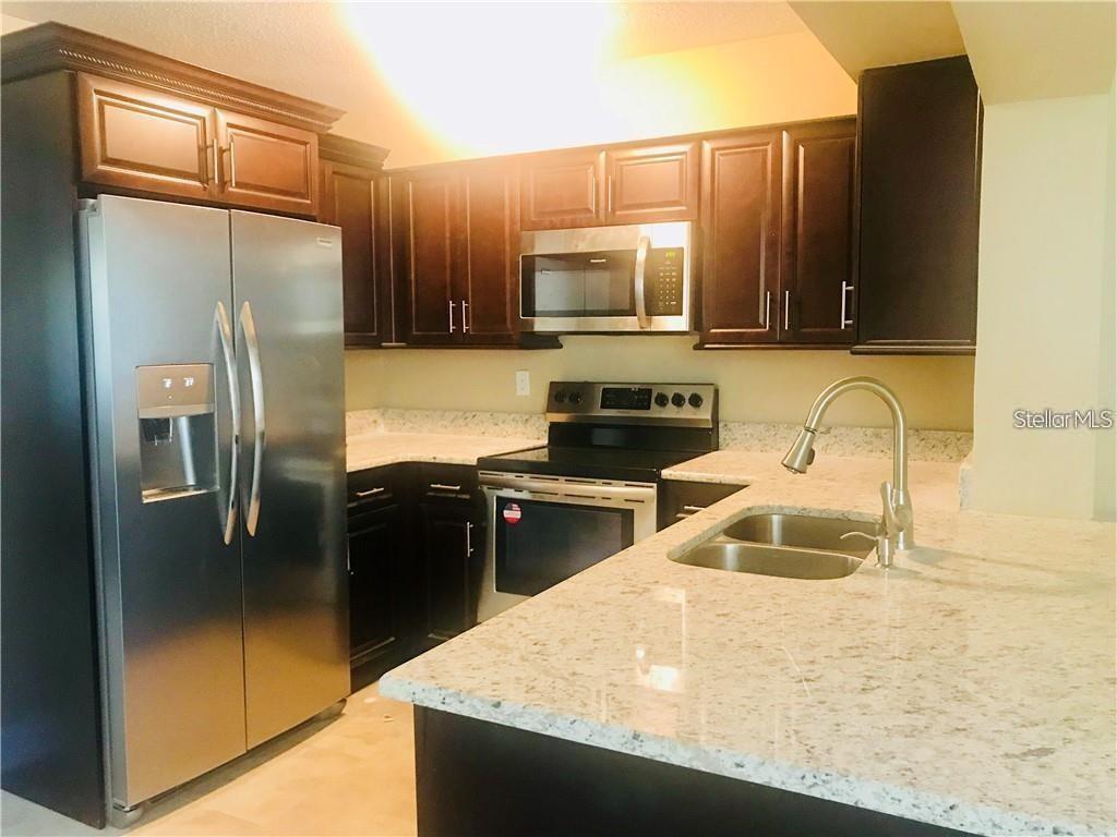 A kitchen features dark wood cabinets, stainless steel appliances, and light-colored granite countertops — 23 COLLEGE DRIVE, BABSON PARK, FL