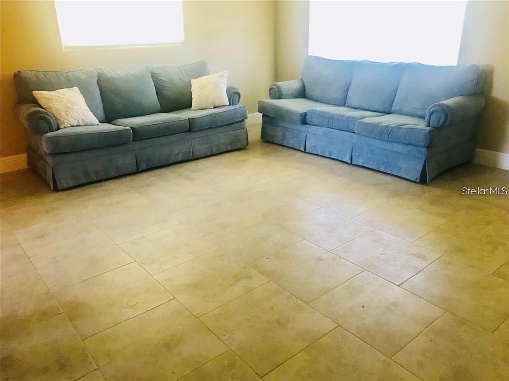 Two blue sofas sit on a light-colored tiled floor in an empty room — 23 COLLEGE DRIVE, BABSON PARK, FL