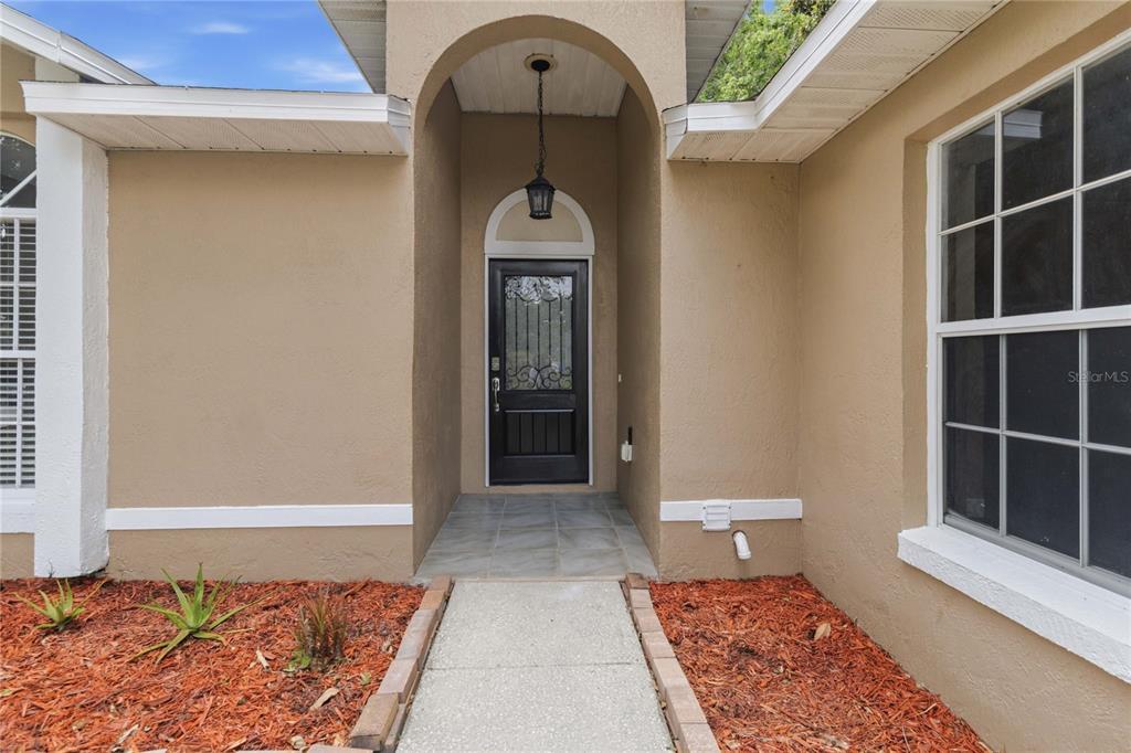 A concrete walkway leads to the front entrance of a house with a black door — 1564 CYPRESS WOODS CIRCLE, ST CLOUD, FL