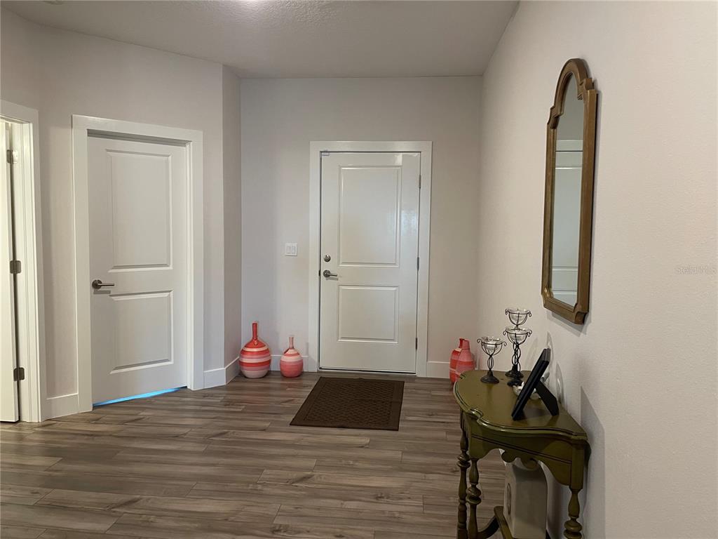 An entryway features light wood-look flooring, white doors, a wall mirror, and a console table — 13084 MOTMOT ROAD, WEEKI WACHEE, FL