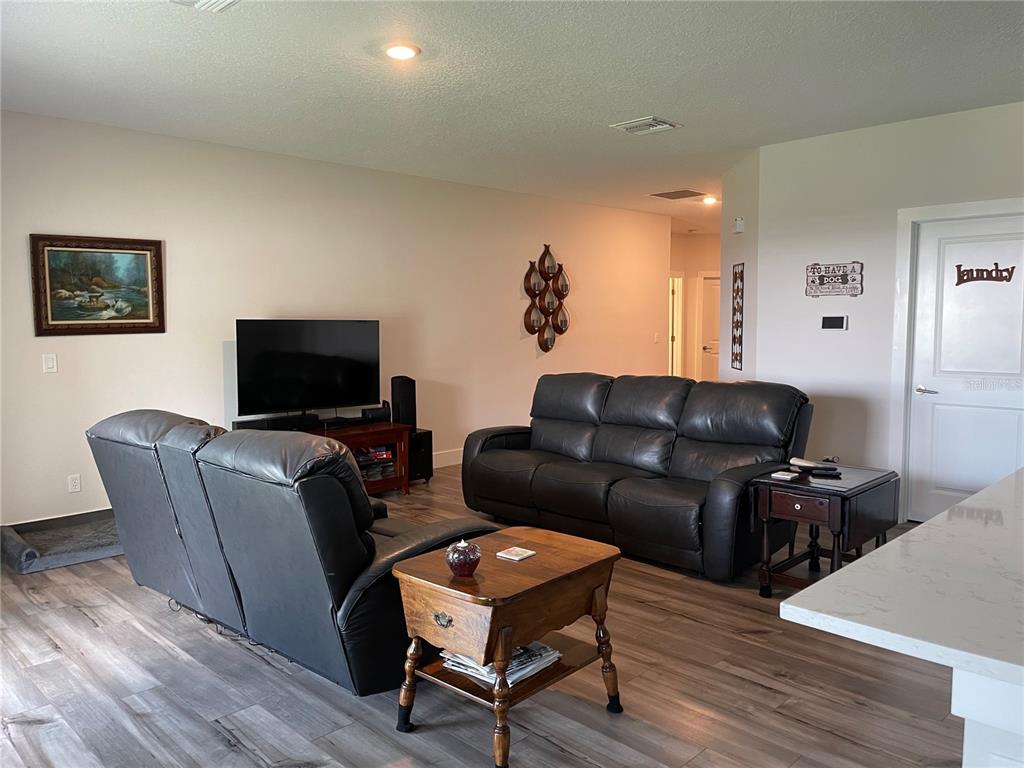 A living room features a dark leather sofa and recliner, wood-look flooring, and a television — 13084 MOTMOT ROAD, WEEKI WACHEE, FL