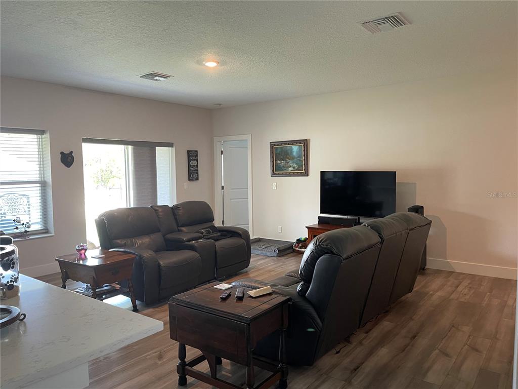 A living room features dark leather recliners, wood-look flooring, and a television on a stand — 13084 MOTMOT ROAD, WEEKI WACHEE, FL