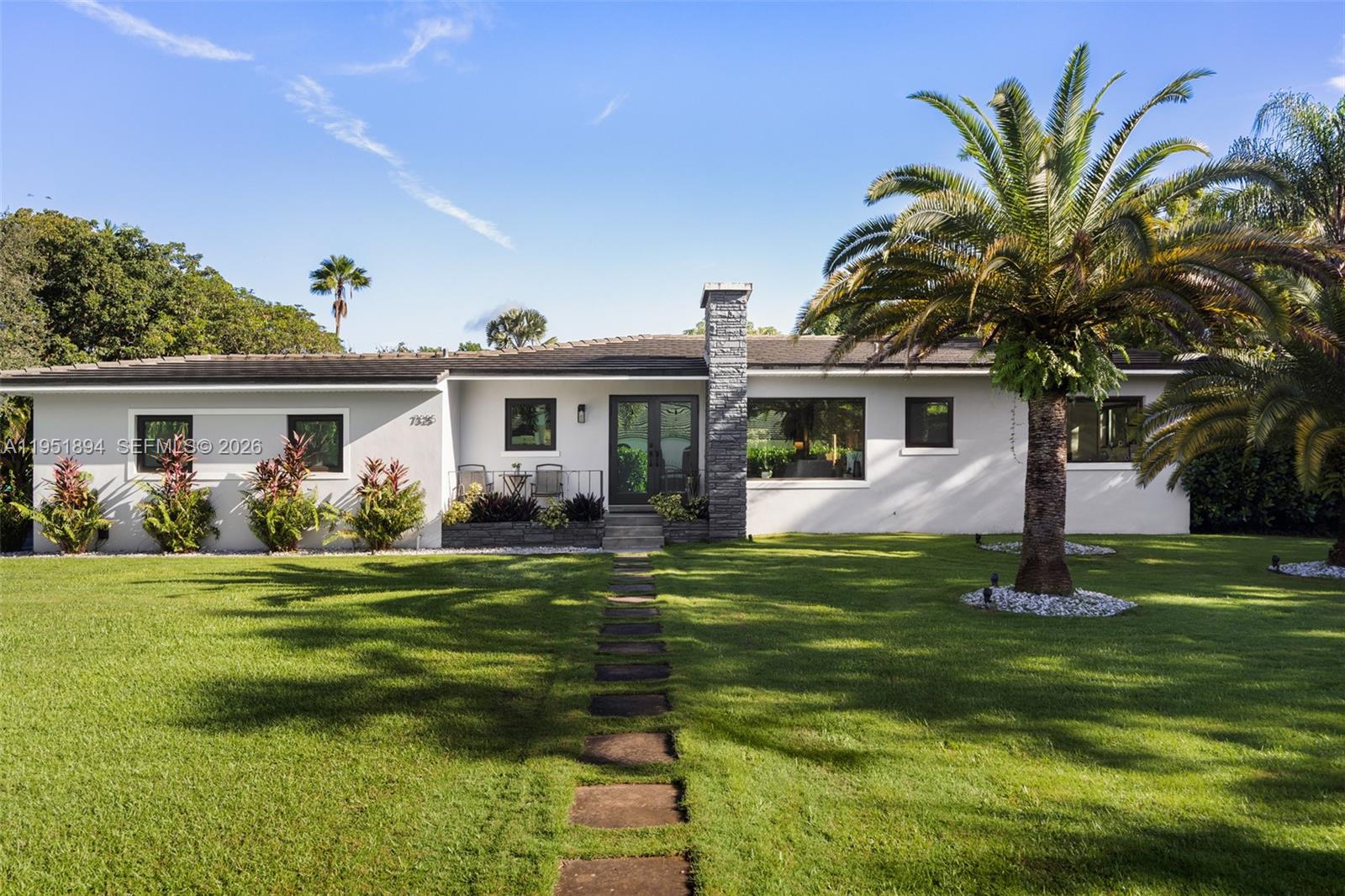 A single-story white house features a stone chimney, a stone walkway, and a large palm tree — 07325 SW 102nd St, Pinecrest FL 33156, PINECREST, FL