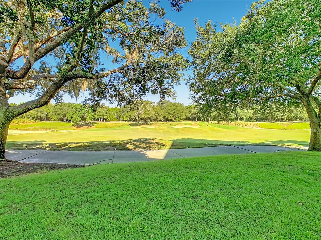 A view of a golf course fairway framed by large oak trees and a paved path — 1358 CENTRE COURT RIDGE DRIVE UNIT 101, REUNION, FL