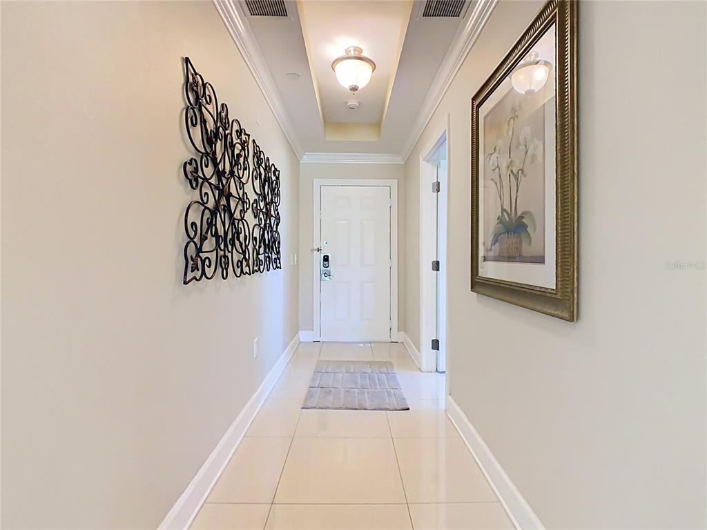 A bright hallway features light tile flooring, a tray ceiling, and decorative wall art — 1358 CENTRE COURT RIDGE DRIVE UNIT 101, REUNION, FL