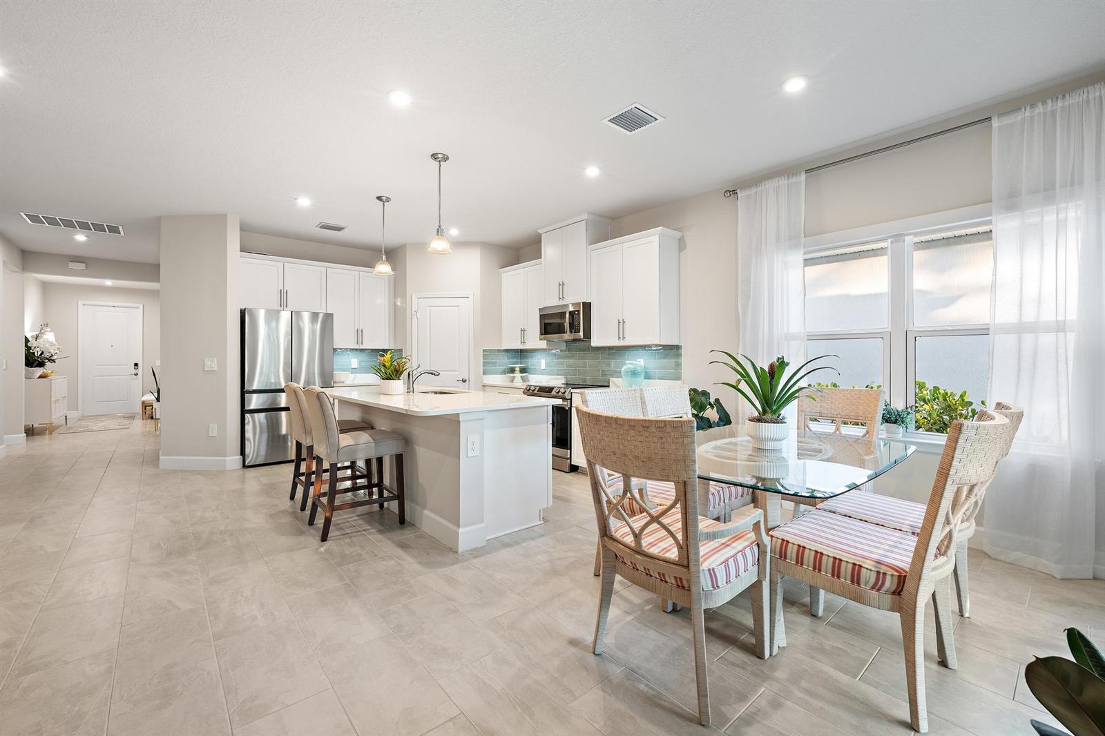 A modern kitchen features white cabinetry, a central island with bar seating, and a dining area — 178 SW Pomeroy Street, Stuart FL 34997, STUART, FL
