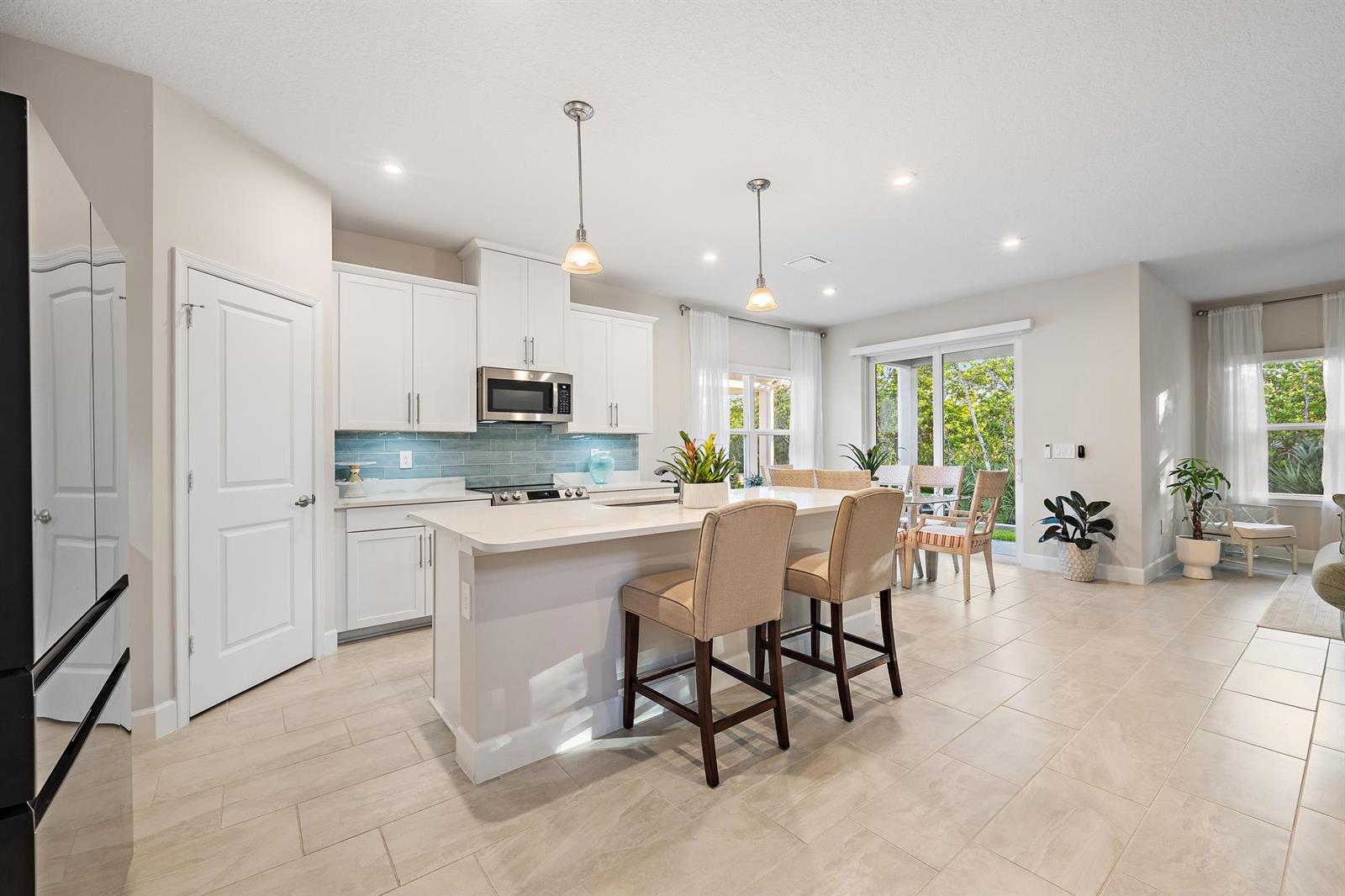 A modern kitchen features white cabinetry, a quartz island with bar stools, and tile flooring — 178 SW Pomeroy Street, Stuart FL 34997, STUART, FL