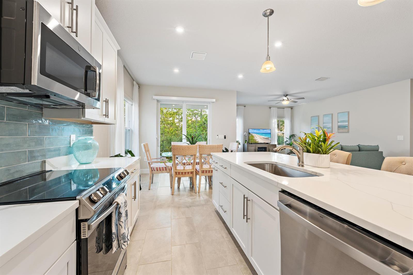A modern kitchen features white cabinets, quartz countertops, stainless steel appliances, and a dining area — 178 SW Pomeroy Street, Stuart FL 34997, STUART, FL