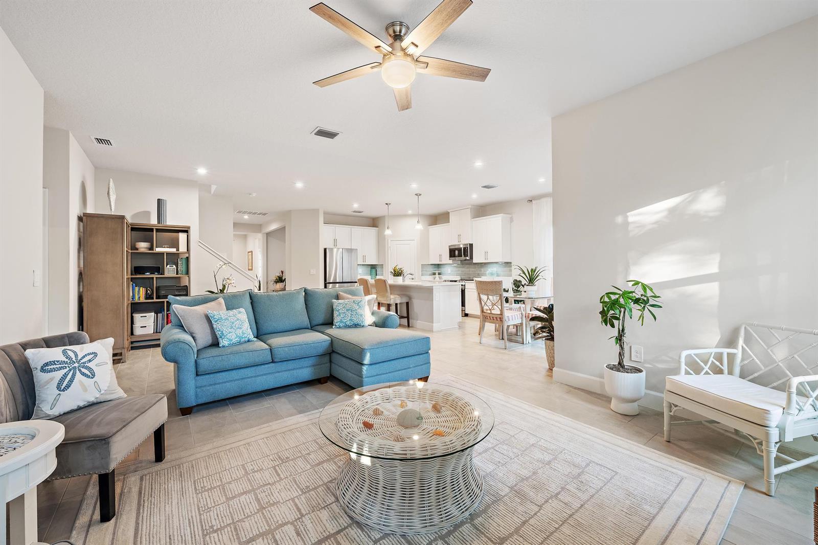 A bright living room features a blue sectional sofa, a glass-topped wicker table, and an open kitchen — 178 SW Pomeroy Street, Stuart FL 34997, STUART, FL