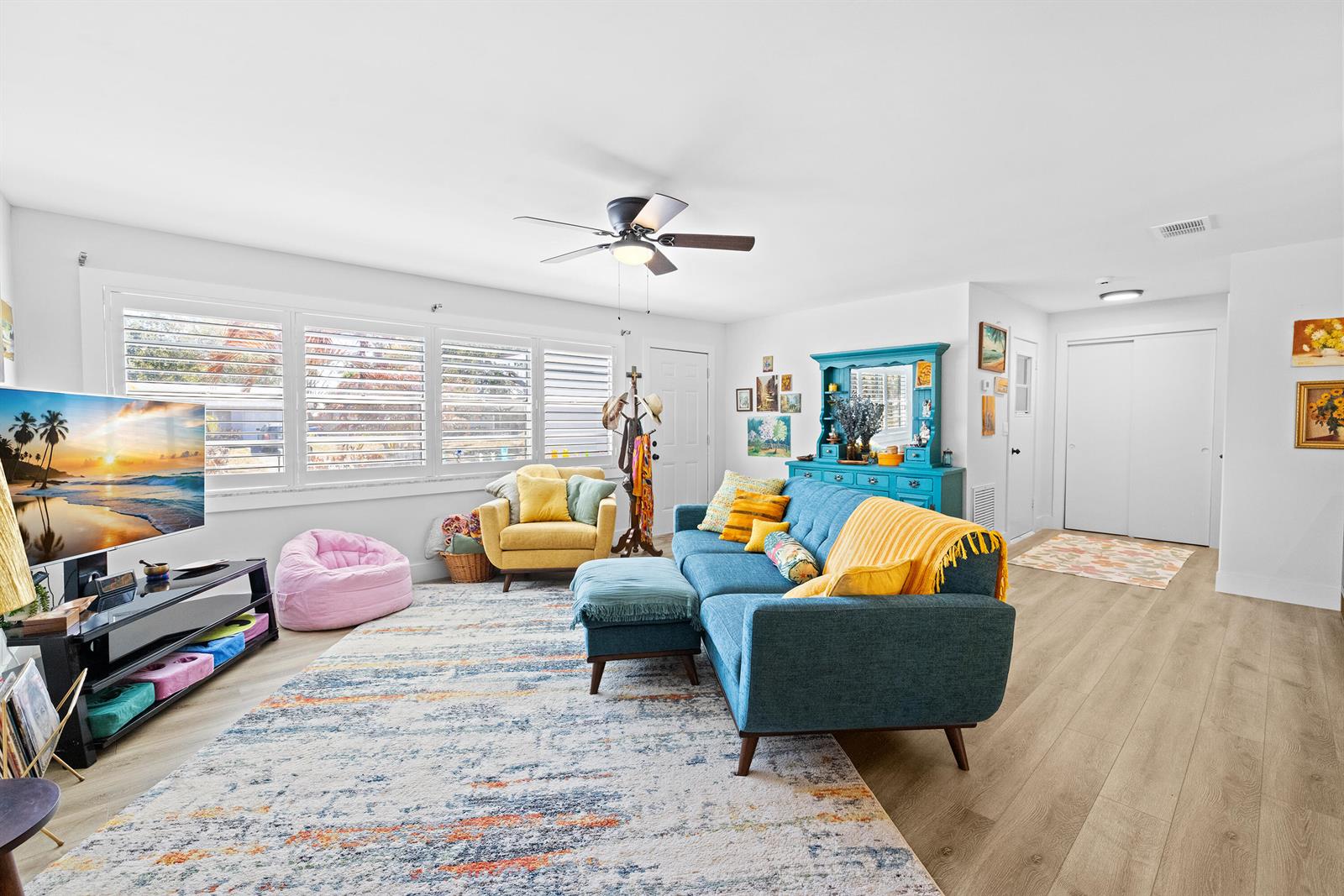 A living room features a blue sofa, yellow armchair, pink beanbag, and a large area rug — 221 Caprol Lane, Sebastian FL 32958, SEBASTIAN, FL