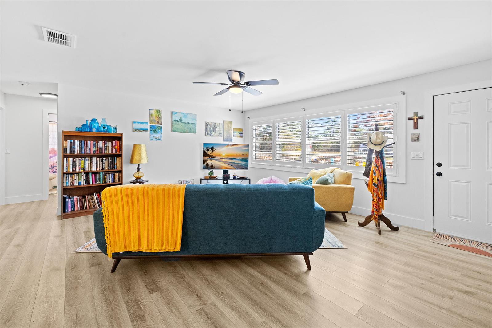 A living room features a blue sofa, a yellow armchair, a bookshelf, and light flooring — 221 Caprol Lane, Sebastian FL 32958, SEBASTIAN, FL