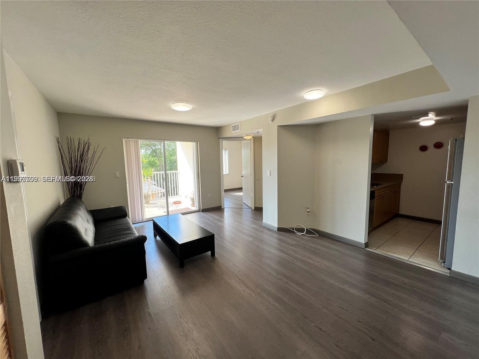 A living room with wood-look flooring, a black sofa, and an adjacent kitchen area — 637 SW 3rd St # 306, Miami FL 33130, MIAMI, FL
