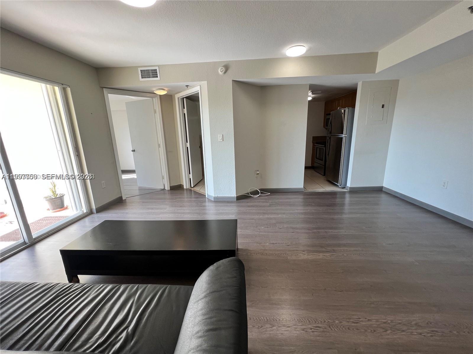 A living room with wood-look flooring, a sliding glass door, and an adjacent kitchen area — 637 SW 3rd St # 306, Miami FL 33130, MIAMI, FL