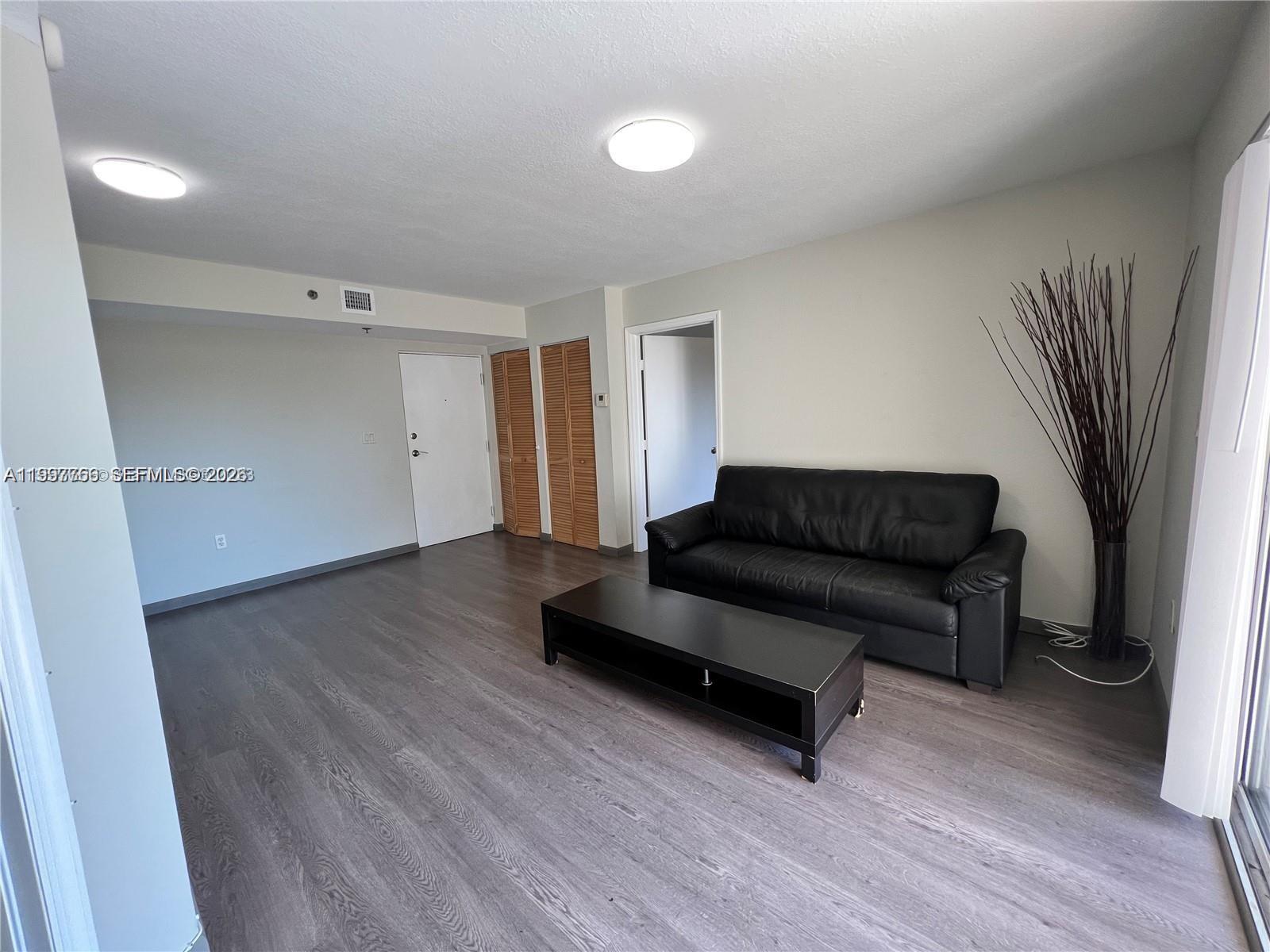 A living room features gray wood-look flooring, a black sofa, and a matching coffee table — 637 SW 3rd St # 306, Miami FL 33130, MIAMI, FL