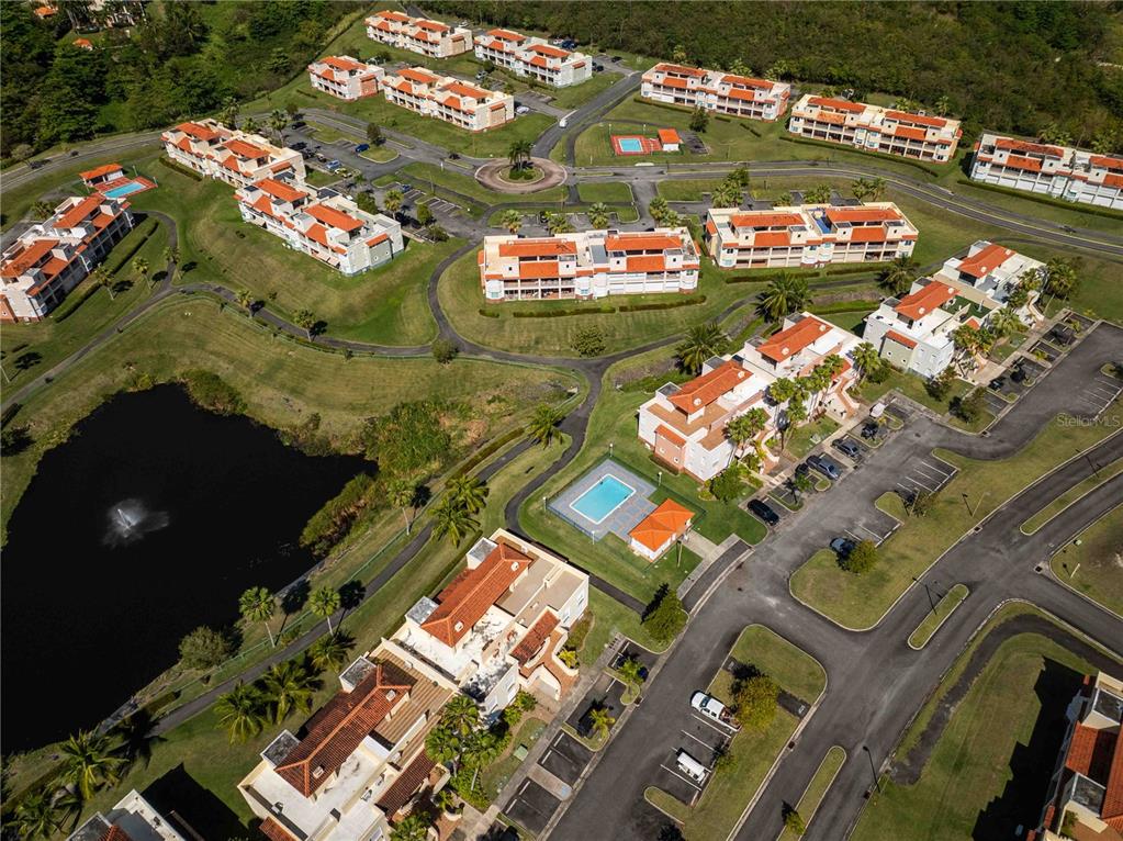 An aerial view shows multiple apartment buildings with red roofs surrounding a pond and pools — 180 PALMAS DRIVE UNIT 60-D, HUMACAO, PR