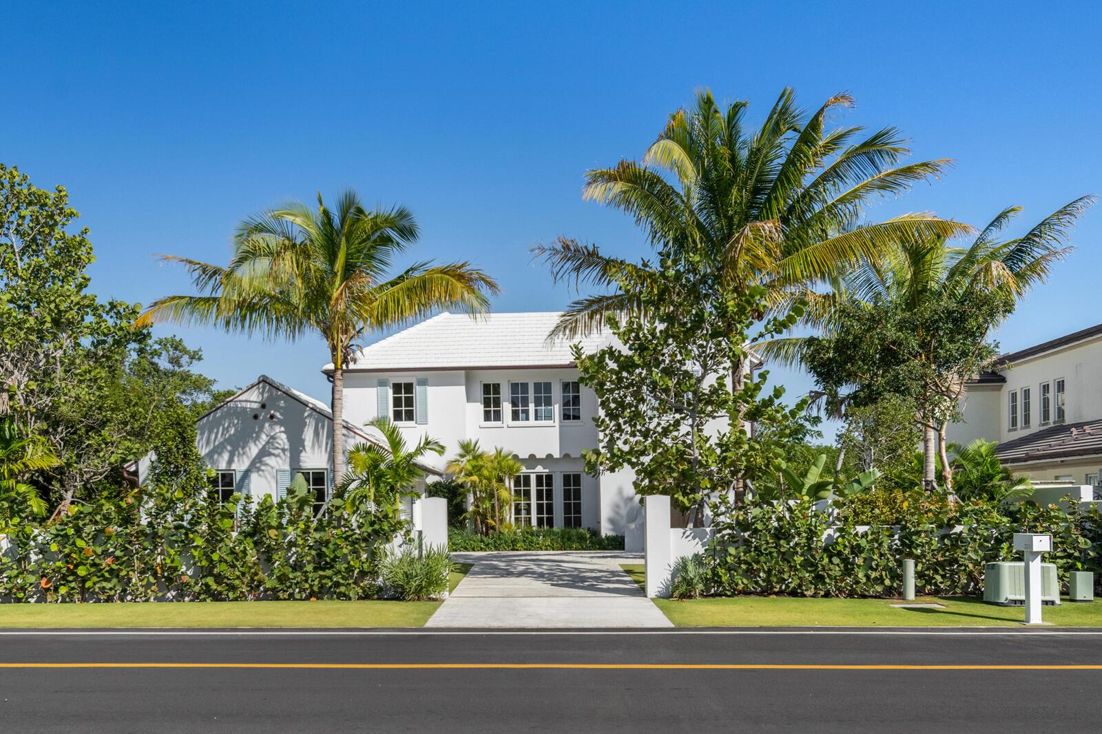 A two-story white house with a tiled roof sits behind a lush garden and driveway — 2219 Ibis Isle Road E, Palm Beach FL 33480, PALM BEACH, FL