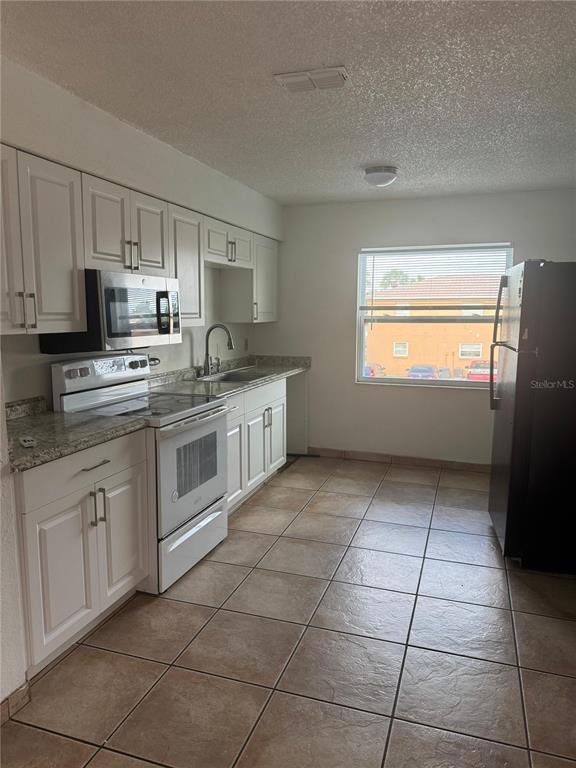 A kitchen features white cabinets, granite countertops, stainless steel appliances, and tan tile flooring — 712 MICHIGAN CT UNIT 3, ST CLOUD, FL