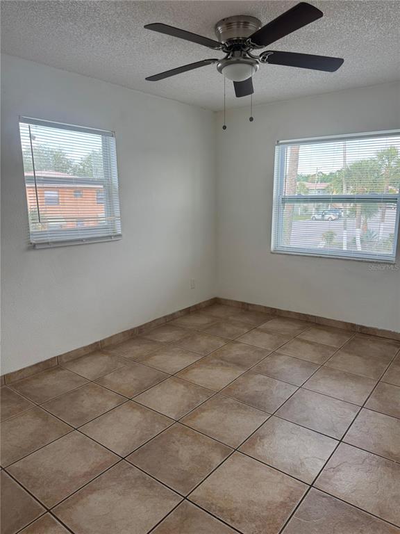 An empty room features beige tile flooring, white walls, two windows with blinds, and a ceiling fan — 712 MICHIGAN CT UNIT 3, ST CLOUD, FL
